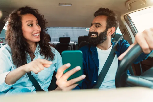 Organizar un plan de coche compartido en la empresa Un conductor y su acompañante consultan un teléfono dentro de un coche