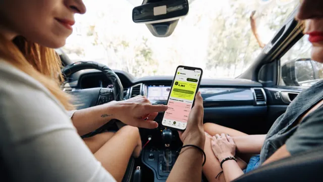 Dos personas consultan una pantalla de La Rueda en un móvil dentro de un coche